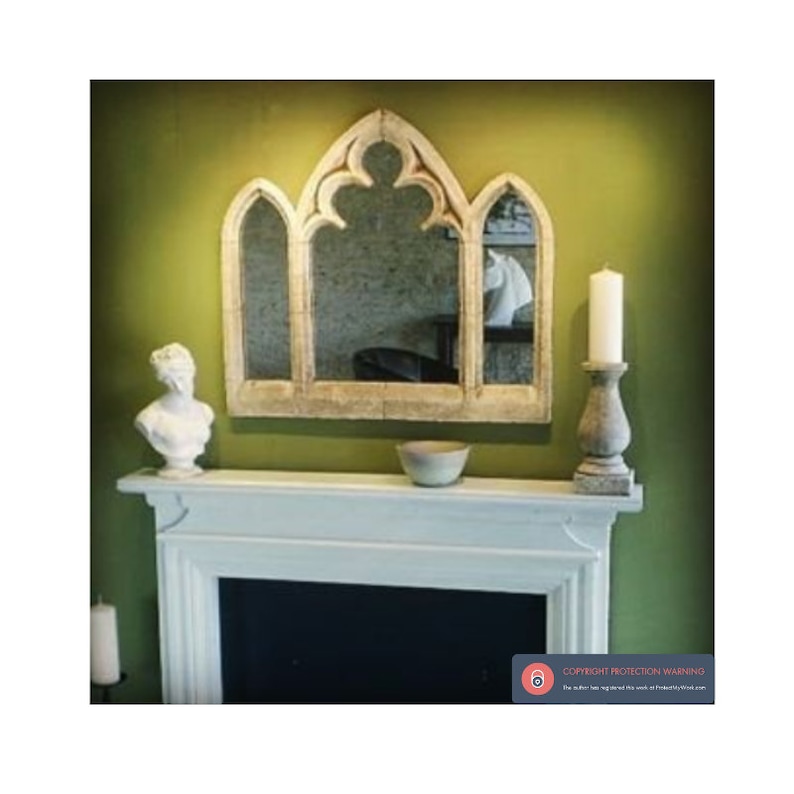 May include: A white, arched, decorative mirror with a gothic design hangs above a white fireplace mantel. The mirror is set against a green wall. A white bust of a woman sits on the mantel, and a small, white bowl sits to the right of the bust. A candle sits on a gray stone candle holder to the right of the bowl.