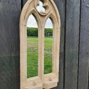 May include: A beige stone-like mirror with a gothic arch design. The mirror has two panes and a decorative detail at the top.