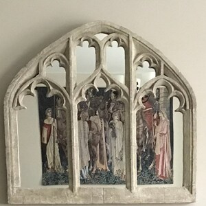 May include: A decorative arched mirror with a faux stone finish. The mirror is divided into five sections with a gothic style design. The mirror reflects a tapestry with a medieval scene.