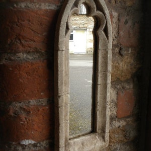 May include: A stone archway with a pointed top and decorative carvings. The archway is set into a brick wall and frames a view of a building with a white door.