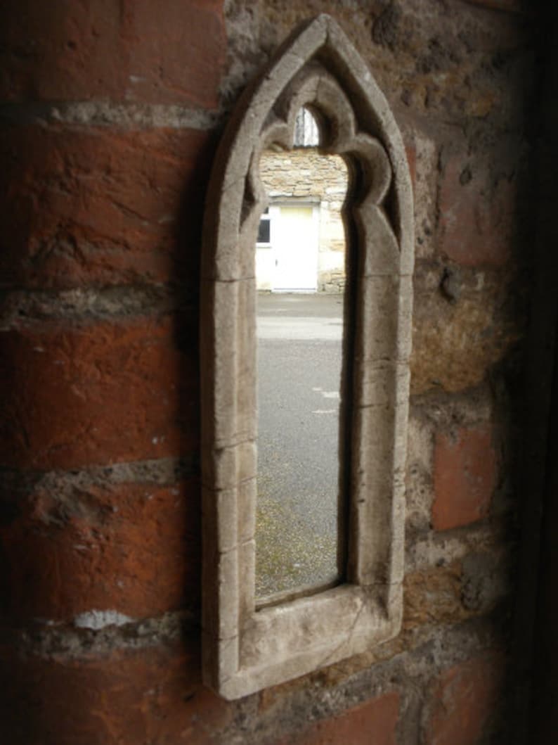 May include: A stone archway with a pointed top and decorative carvings. The archway is set into a brick wall and frames a view of a building with a white door.
