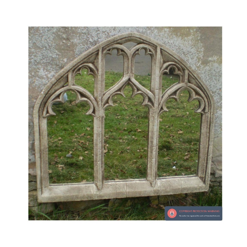 May include: A large, arched, decorative mirror with a stone-like finish. The mirror has a gothic design with multiple arched windows and intricate details. The mirror is reflecting a green lawn.