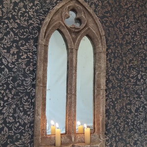 May include: A stone archway mirror with a pointed top and two windows. Three lit candles are placed on the ledge below the windows.