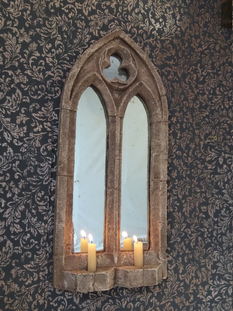 May include: A stone archway mirror with a pointed top and two windows. Three lit candles are placed on the ledge below the windows.