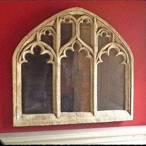 May include: A white wooden arched window frame with a Gothic design. The frame has three arched openings with intricate carvings and a decorative top.