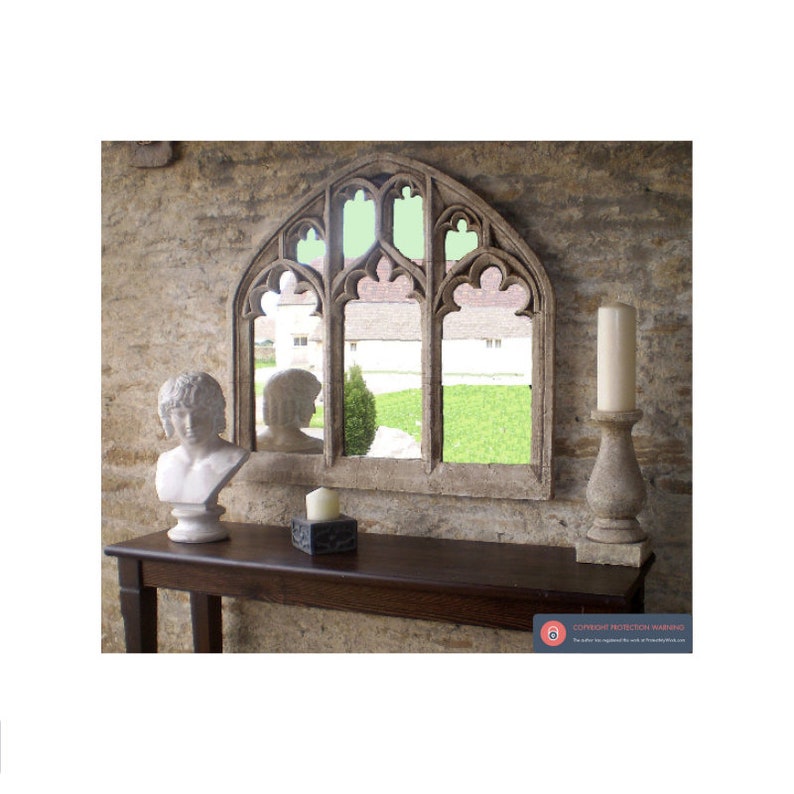 May include: A decorative arched mirror with a stone-like finish, featuring three arched windows with a view of a green lawn and buildings in the reflection. The mirror is displayed on a dark brown wooden table with a white bust sculpture and a candle holder.