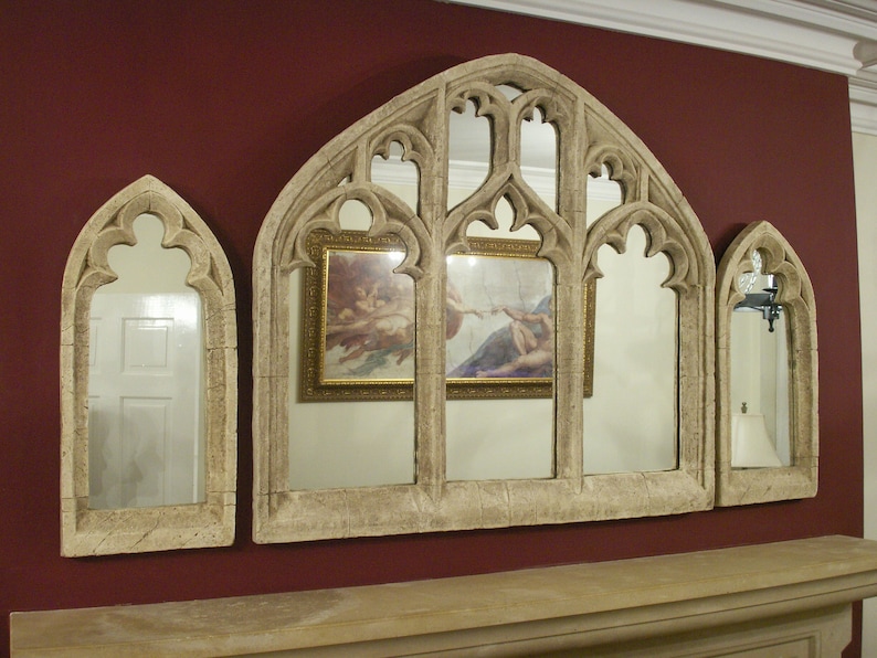 May include: A set of three arched mirrors with ornate frames, each with a different reflection. The center mirror reflects two framed paintings, while the side mirrors reflect a room with a white door. The mirrors are made of a light beige material and have a distressed finish.