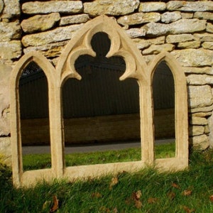 May include: A decorative stone window mirror with a gothic arch design. The mirror has three panels and is made of a light brown stone.