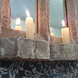 May include: A stone mirror with three lit candles. The mirror is framed with a rough stone texture and has a rectangular shape.