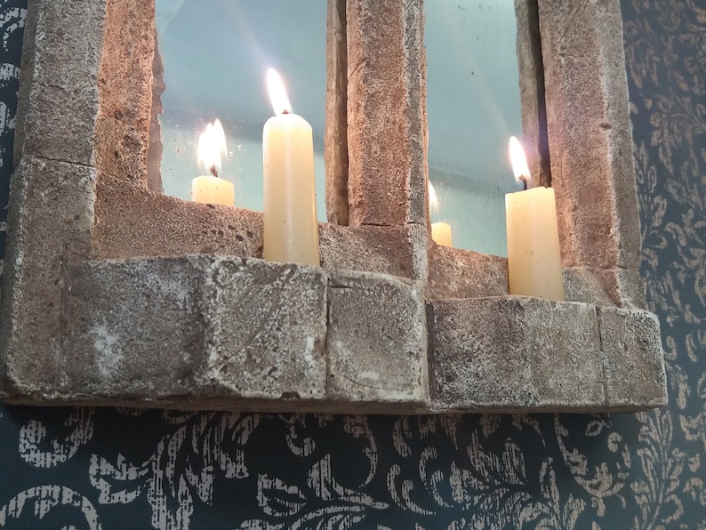May include: A stone mirror with three lit candles. The mirror is framed with a rough stone texture and has a rectangular shape.