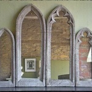 May include: Set of six gray stone arched mirrors of varying sizes. The mirrors are arranged in a row on a wooden surface.