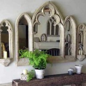 May include: Set of four arched mirrors with a distressed white finish. The mirrors are arranged in a row, with the largest mirror in the center and two smaller mirrors on either side. The mirrors have a gothic style design with pointed arches and intricate details.