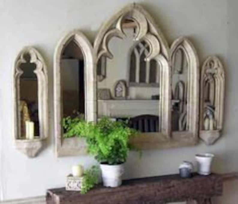 May include: Set of four arched mirrors with a distressed white finish. The mirrors are arranged in a row, with the largest mirror in the center and two smaller mirrors on either side. The mirrors have a gothic style design with pointed arches and intricate details.