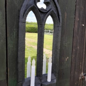 May include: Black gothic style mirror with a pointed arch and a decorative design. The mirror has two candle holders on the bottom.