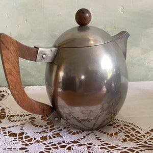 May include: A silver teapot with a wooden handle and a round lid. The teapot has a shiny, reflective surface.