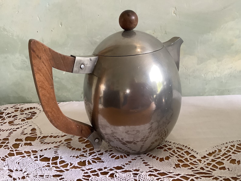 May include: A silver teapot with a wooden handle and a round lid. The teapot has a shiny, reflective surface.