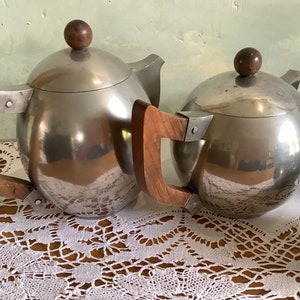 May include: A set of three silver teapots with wooden handles. The teapots have a round, spherical shape and a shiny, reflective surface.
