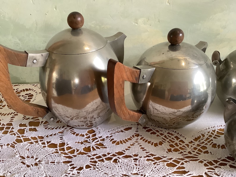 May include: A set of three silver teapots with wooden handles. The teapots have a round, spherical shape and a shiny, reflective surface.