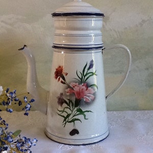 May include: White enamel coffee pot with a floral design featuring pink and purple flowers. The pot has a blue and white lid and a blue rim.