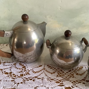 May include: A silver tea set with wooden handles. The set includes a teapot, a sugar bowl, and a creamer.