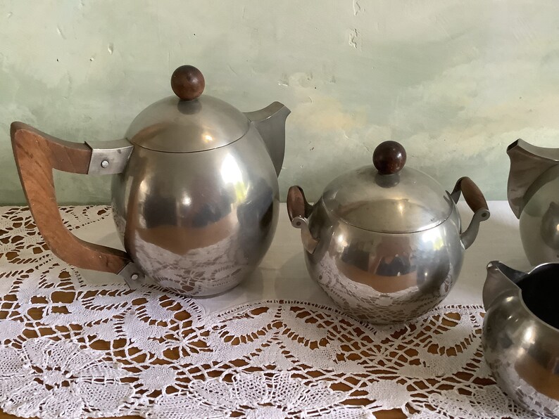 May include: A silver tea set with wooden handles. The set includes a teapot, a sugar bowl, and a creamer.