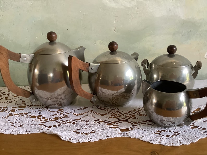 May include: A silver tea set with wooden handles. The set includes a teapot, a sugar bowl, and a creamer.