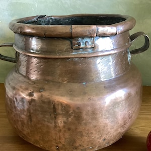 May include: A large, antique copper pot with two handles. The pot has a hammered finish and is slightly dented.