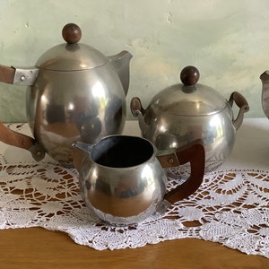 May include: A silver tea set with a teapot, creamer, and sugar bowl. The set has wooden handles and a polished finish.