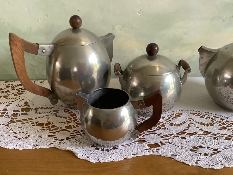 May include: A silver tea set with a teapot, creamer, and sugar bowl. The set has wooden handles and a polished finish.