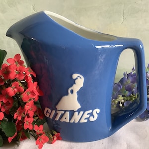 May include: A blue ceramic pitcher with a white silhouette of a woman and the word "Gitanes" in white lettering.