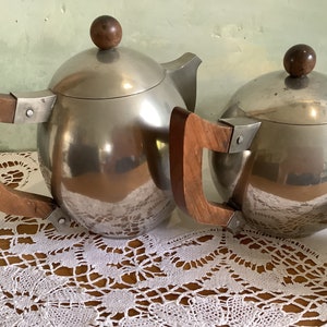 May include: Two silver teapots with wooden handles. The teapots have a round, spherical shape and a shiny, polished finish.