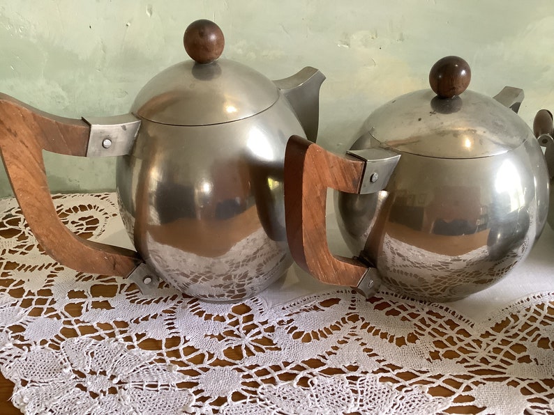 May include: Two silver teapots with wooden handles. The teapots have a round, spherical shape and a shiny, polished finish.