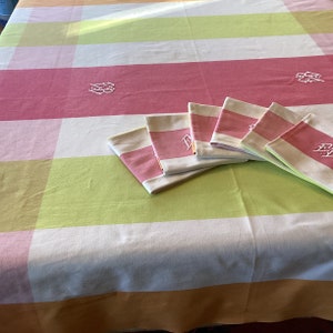 May include: A set of six pink and white striped napkins with embroidered initials. The napkins are arranged on a pink, white, and green checkered tablecloth.