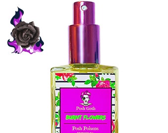 May include: A clear glass bottle with a pink spray top and a black and white striped label. The label features a cartoon illustration of a woman with pink hair and a black choker. The text on the label reads "Posh Goth Burnt Flowers Posh Poisons Perfume Oil Net Weight 30 ml (1 oz)"