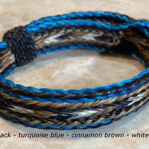 Puede incluir: Un brazalete de cuero trenzado con hilos azul turquesa, marr&oacute;n canela, blanco y negro. El brazalete est&aacute; etiquetado con el n&uacute;mero #17.