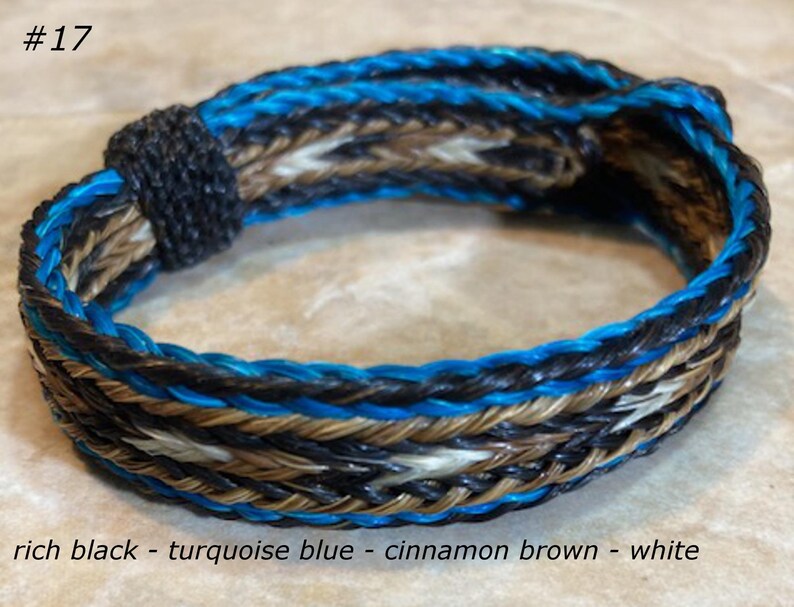 Puede incluir: Un brazalete de cuero trenzado con hilos azul turquesa, marr&oacute;n canela, blanco y negro. El brazalete est&aacute; etiquetado con el n&uacute;mero #17.