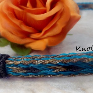 May include: A turquoise, brown, and black braided horsehair rope halter with a brown horsehair tassel. The halter is braided with a knot pattern and has a decorative knot at the end of the tassel. Knot-a-Tail.com is printed on the halter.