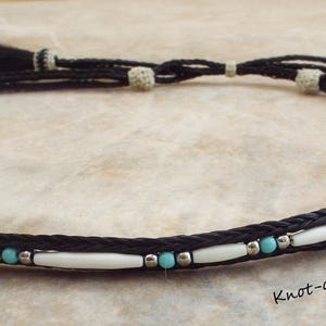 May include: A black horsehair rope necklace with white and turquoise beads. The necklace has tassels on each end. "Knot-a-Tail.com" is printed on the surface.