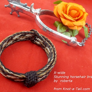 Puede incluir: Un brazalete trenzado de crin de caballo en negro, marr&oacute;n y blanco con un cierre de nudo negro. El brazalete est&aacute; etiquetado como "X-ancho Impresionante brazalete de crin de caballo por roberta de Knot-a-Tail.com".