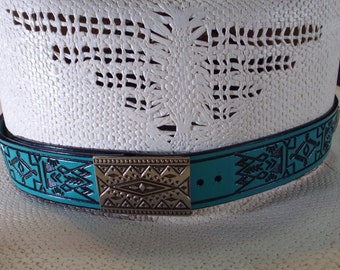 May include: A turquoise leather hat band with a silver buckle featuring a geometric design. The band is decorated with a repeating pattern of stylized arrows.