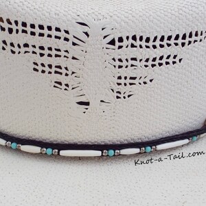 May include: White cowboy hat with a black and white beaded hatband. The hatband features turquoise beads and white beads. The hat has a cut-out design on the crown. The text "Knot-a-Tail.com" is printed on the hat.