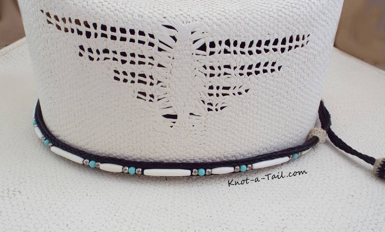 May include: White cowboy hat with a black and white beaded hatband. The hatband features turquoise beads and white beads. The hat has a cut-out design on the crown. The text "Knot-a-Tail.com" is printed on the hat.