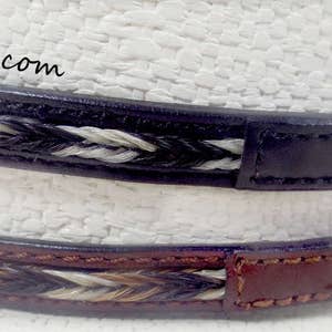May include: Two leather belts with braided horsehair accents. The top belt is black leather with white and black horsehair. The bottom belt is brown leather with white, black, and brown horsehair.