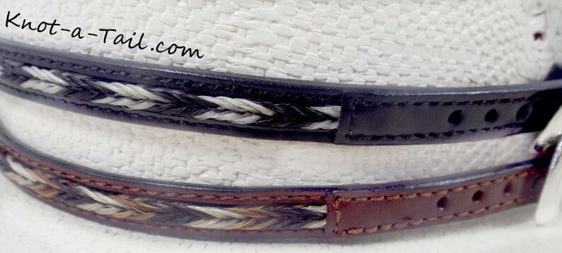 May include: Two leather belts with braided horsehair accents. The top belt is black leather with white and black horsehair. The bottom belt is brown leather with white, black, and brown horsehair.