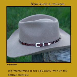 May include: A tan cowboy hat with a brown leather and horsehair hat band. The hat band has a silver buckle. The hat is sitting on a wooden surface.