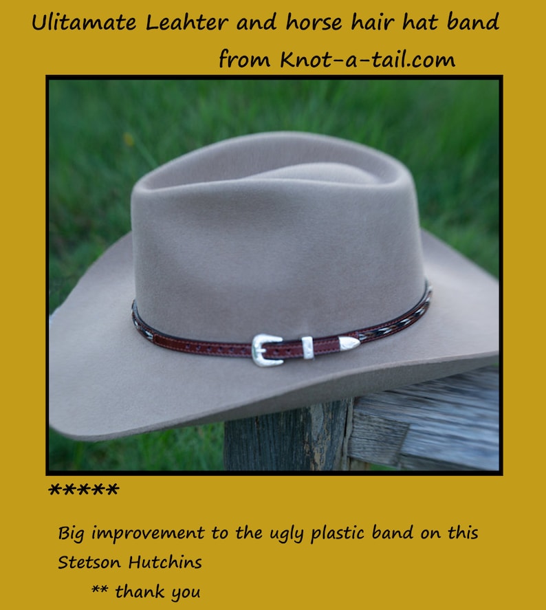 May include: A tan cowboy hat with a brown leather and horsehair hat band. The hat band has a silver buckle. The hat is sitting on a wooden surface.