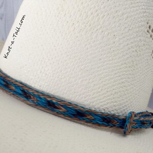 May include: A turquoise, brown, and black braided leather hat band with a long tail. The hat band is on a white cowboy hat.