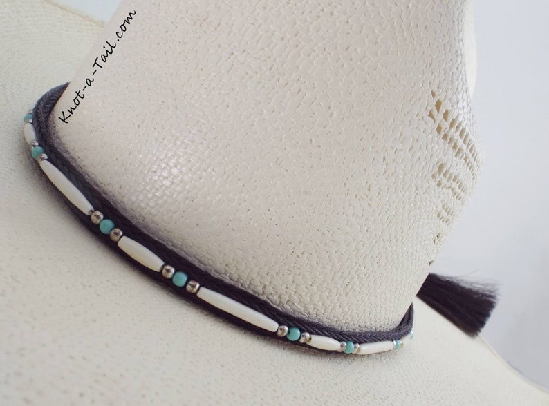 May include: A white cowboy hat with a black hat band and turquoise and white beads. The hat band has the text "Knot-a-Tail.com" on it.