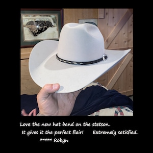 May include: A white cowboy hat with a black and white hat band. The hat is being held by a person's hand. The text "Love the new hat band on the stetson. It gives it the perfect flair! ***** Robyn Extremely satisfied." is visible at the bottom of the image.