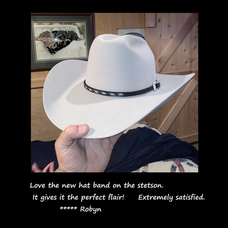 May include: A white cowboy hat with a black and white hat band. The hat is being held by a person's hand. The text "Love the new hat band on the stetson. It gives it the perfect flair! ***** Robyn Extremely satisfied." is visible at the bottom of the image.
